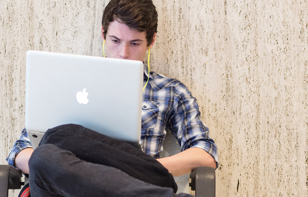 male student working on a Macbook with earbuds in
