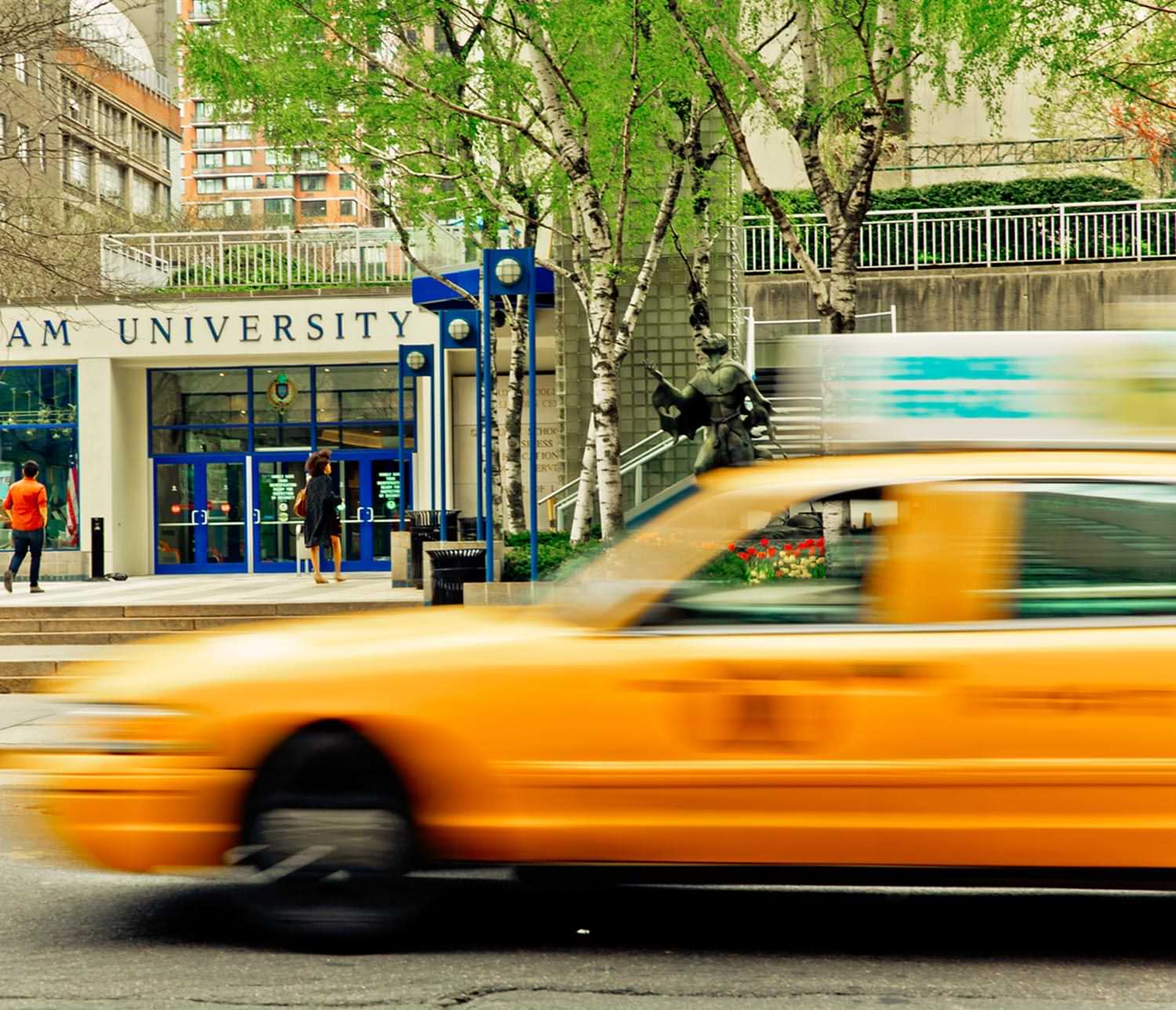 a taxi passes on a street in front a Fordham University building