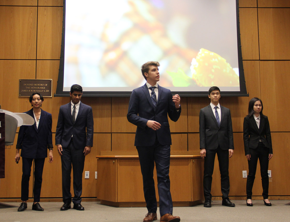 five students in suits front of a projector giving their presentation