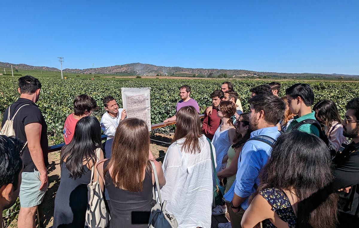 Undergraduate students from Fordham Gabelli School of Business toured a Chilean vineyard as they all gather together outside glancing upon a map showing the numerous different points of interest throughout the vineyard on a bright clear sunny day.