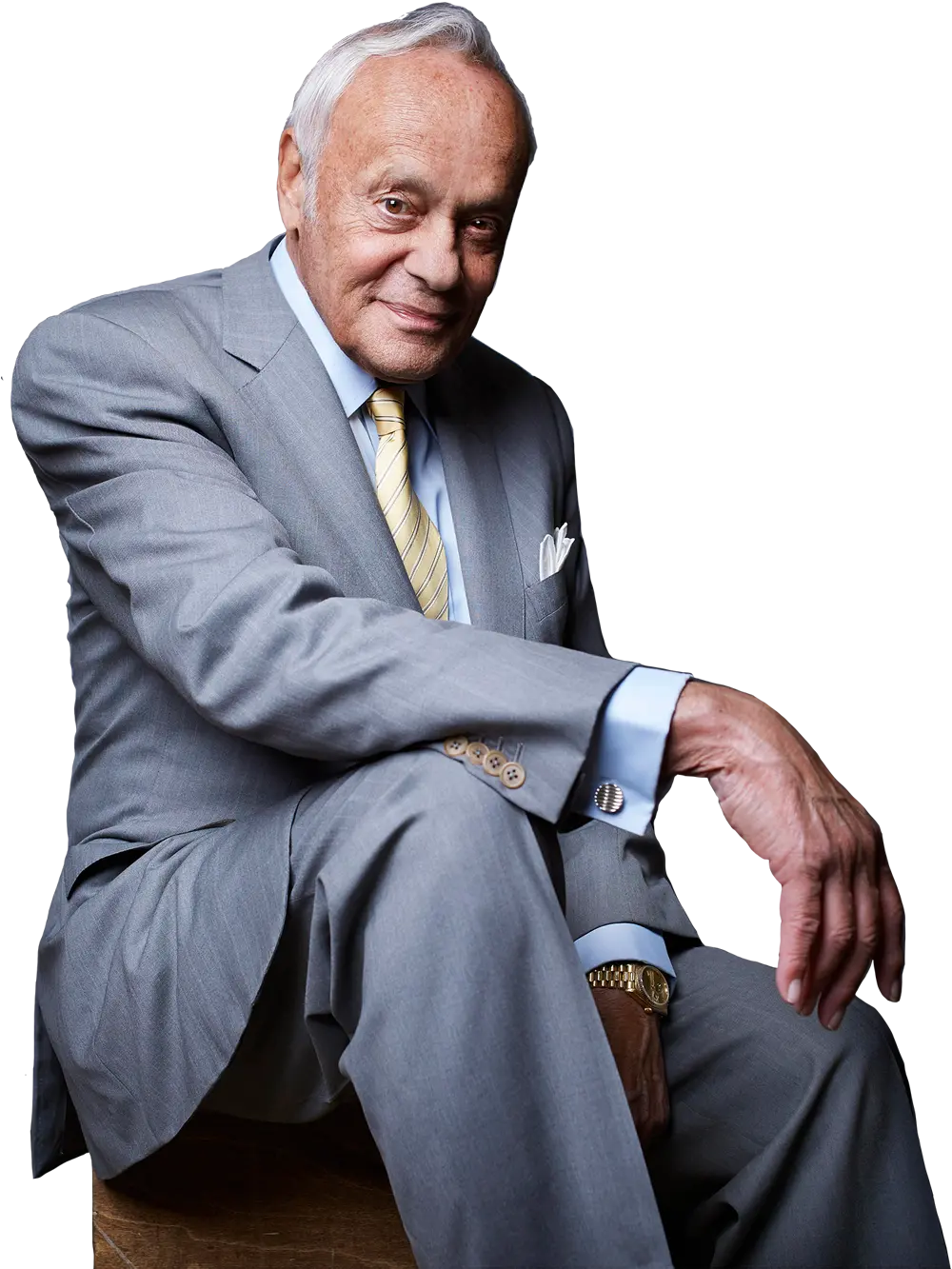 seated portrait image of Spiros “Sig” Segalas wearing a grey pinstriped suit with a pastel yellow pinstriped tie