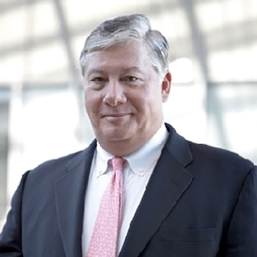 Portrait headshot close-up photo of Donald V. Almeida grinning in a black business blazer suit and white button-up dress shirt underneath equipped with a pink tie