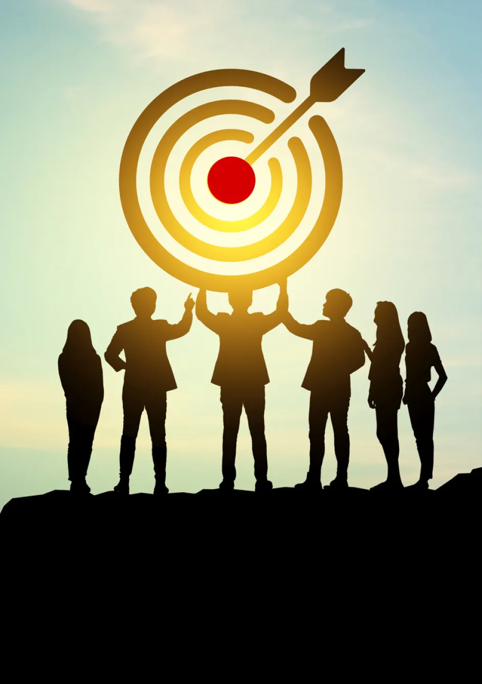 Silhouettes of six people standing on a hill, lifting a large target with an arrow hitting the bullseye, symbolizing teamwork, goal achievement, and success against a bright sky background.