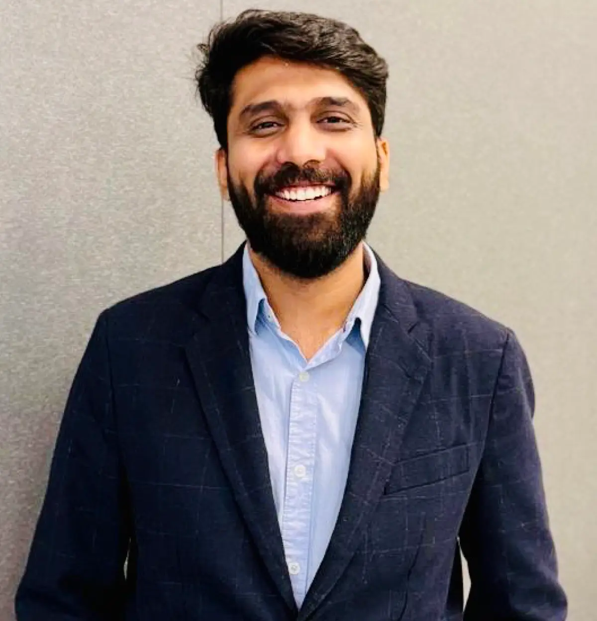 Portrait orientation headshot photograph of Harsh Thakkar (Gabelli '25, President, Gabelli School Graduate Student Advisory Council, Graduate Diploma Ceremony Speaker, Entrepreneur) smiling with a full dark black beard plus dark black wavy short hair dressed in a dark navy blue plaid business suit blazer with a light sky blue button-up dress shirt underneath