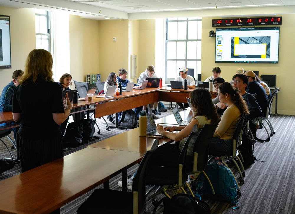 A classroom with students around a U-shaped table and a teacher standing in front.