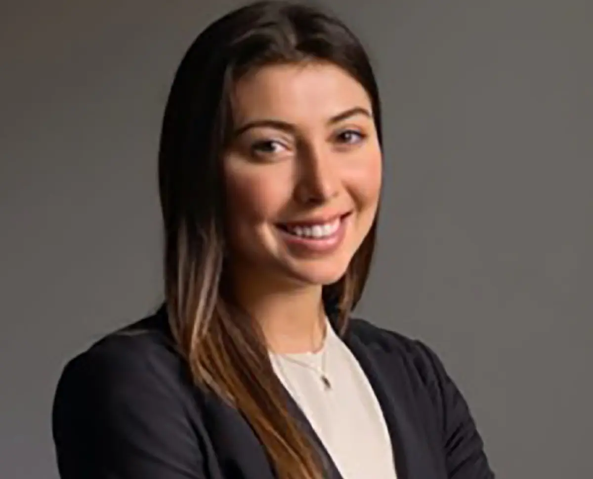 Headshot photograph of Catherine Polisano, a woman smiling in a black business blazer suit and dark beige tan dress shirt underneath with a thin necklace equipped