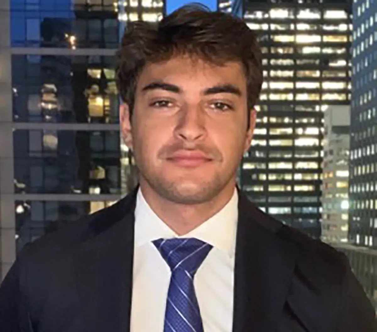 Headshot photograph of Vittorio Torghele, a man grinning in a black business blazer suit and white button-up dress shirt underneath with a dark blue tie equipped