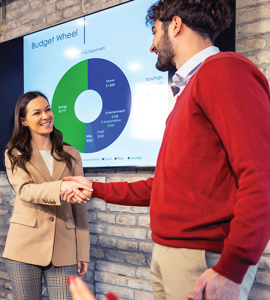 Two professionals shaking hands in front of a screen displaying a "Budget Wheel" financial chart.